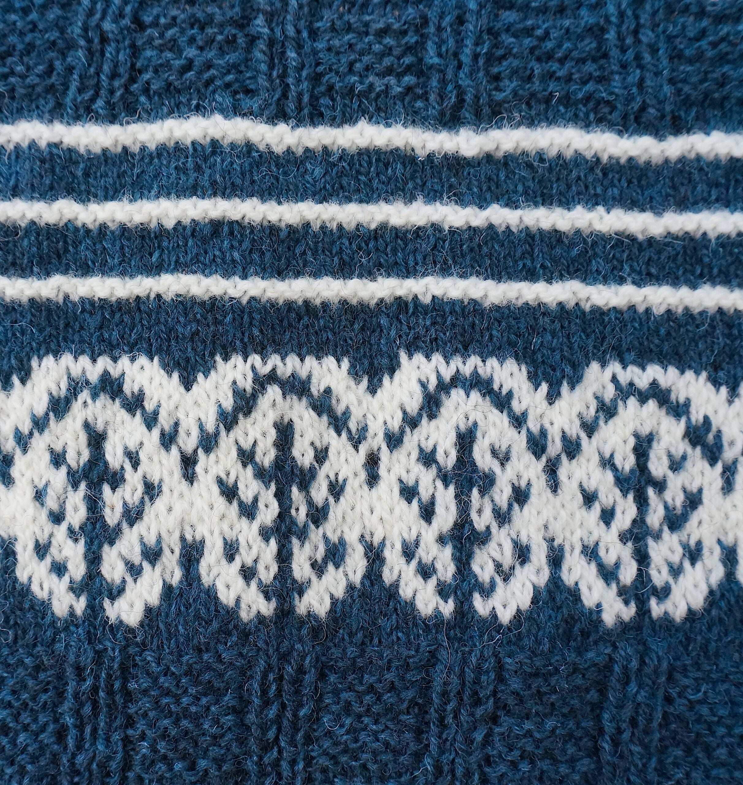 close up of Pottery Tree Wrist Warmers and Cowl Pattern by Emma Vining. They have a knitted motif of a tiny tree within a white oval and white stripes on blue.