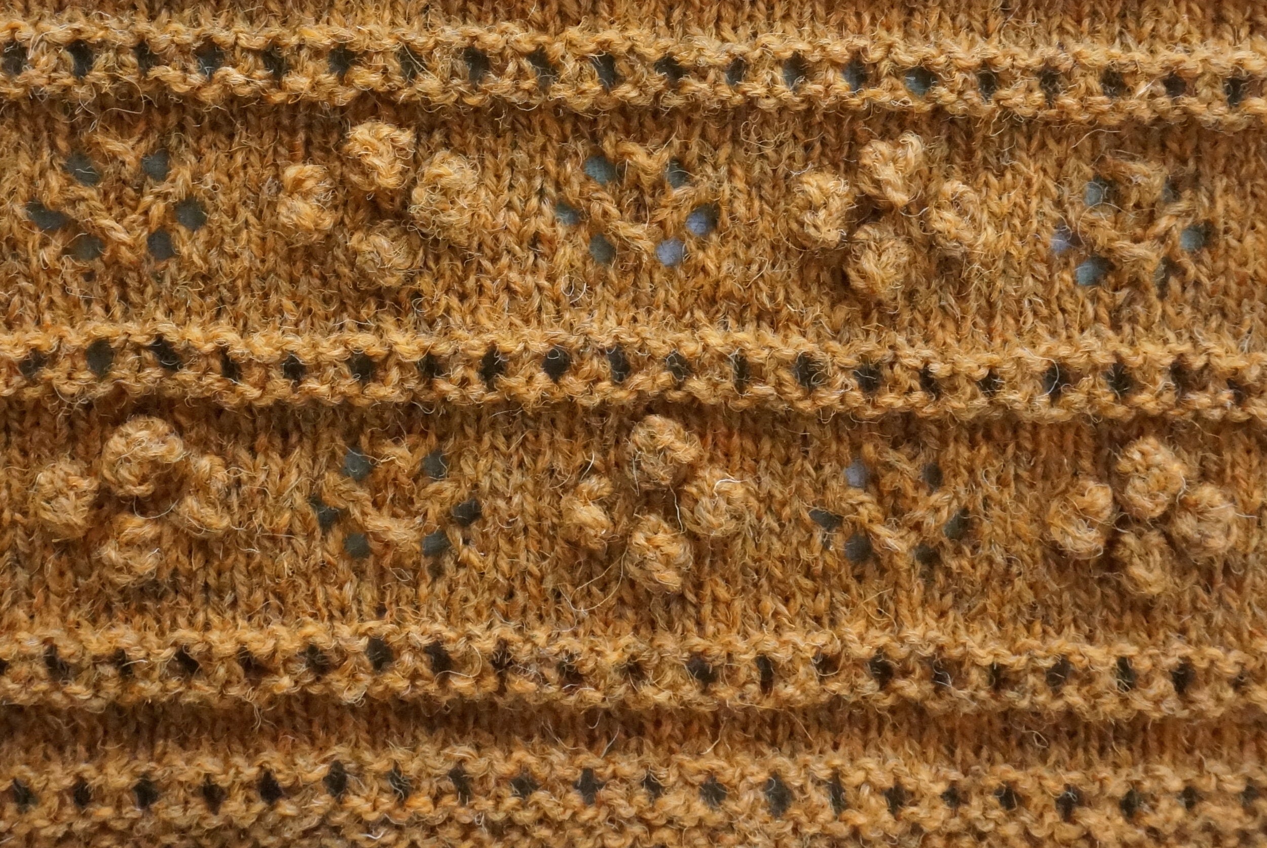 Machair Wildflower Shawl in orange yarn with lace eyelets and raised bobbles detail
