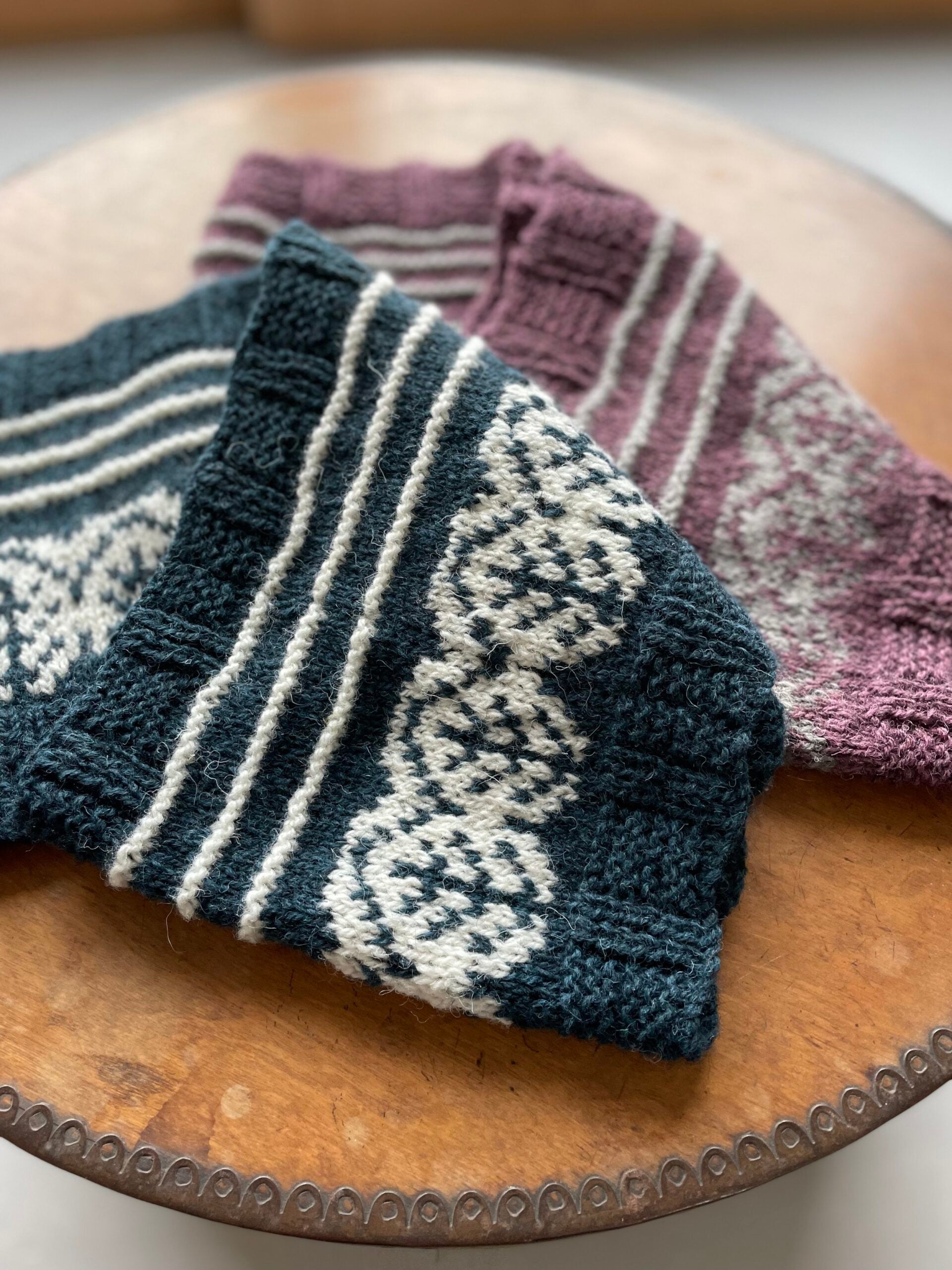  Pottery Tree  Cowl Pattern by Emma Vining. They have a knitted motif of a tiny tree within a white oval and white stripes.