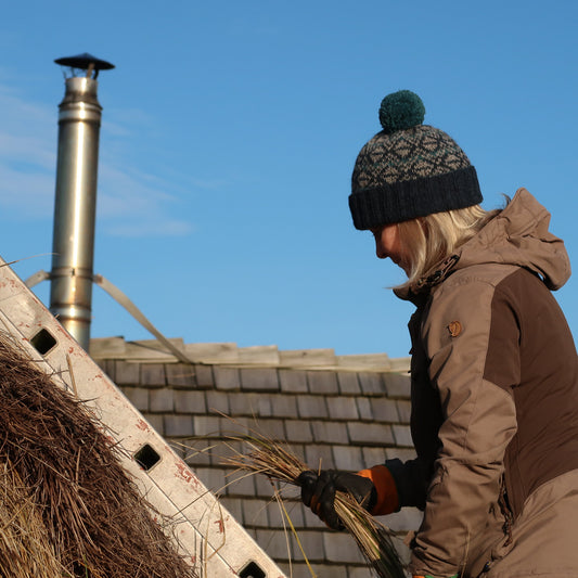 Thatching Hat, beanie with ribbed turn up, colourwork knitting and a bobble worn by Meg outside while thatching
