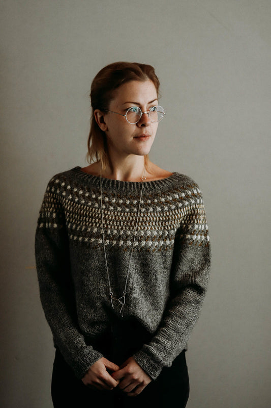 Waterlands sweater designed by Lotta Löthgren. A circular yoke jumper featuring an abstract colour work pattern. Knitted here in greys, white and browns.