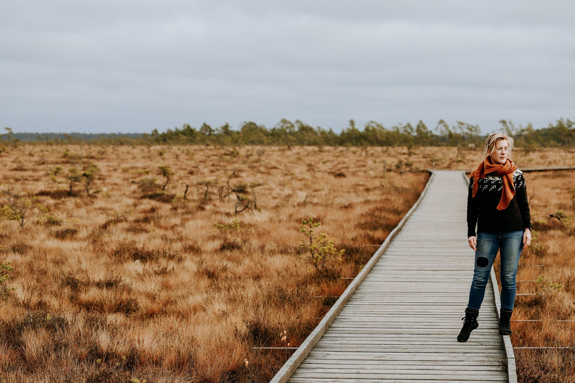 Salix Alba sweater with a circular yoke featuring a pattern resembling arrows or branches. Worn outside on a wooden path, styled with jeans